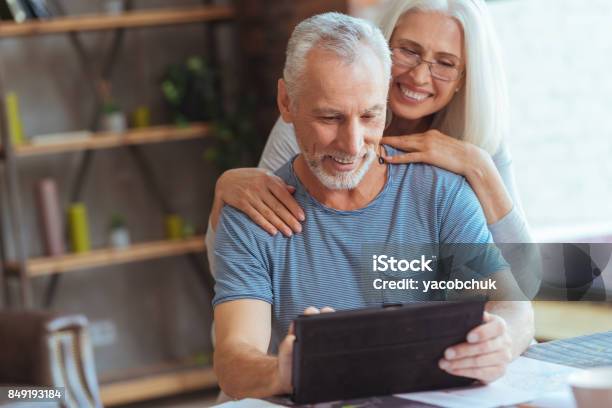 Retired Positive Man Using Tablet With His Wife Stock Photo - Download Image Now - Baby Boomer, Senior Couple, Couple - Relationship