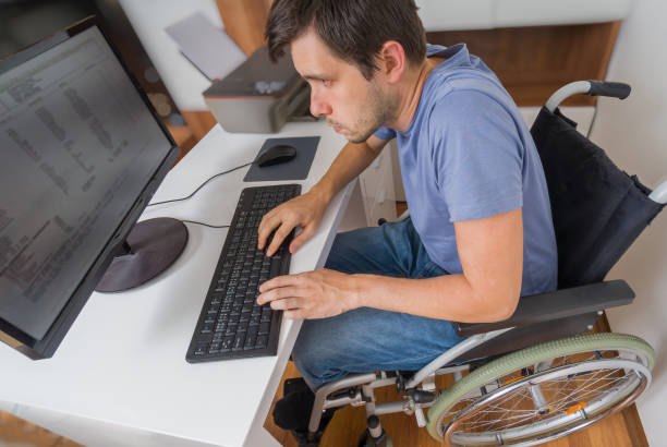 handicapped disabled man on wheelchair is working with computer in office. - physical impairment wheelchair disabled accessibility imagens e fotografias de stock