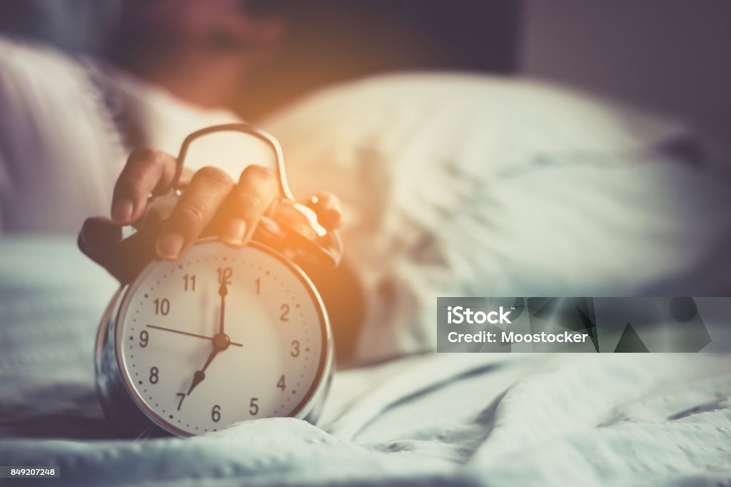 Clock on the bed in the morning. Alarm Clock Stock Photo