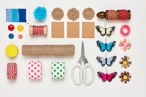 Flat lay of various craft products on white background. Overhead view of art and craft products arranged side by side. Multi colored art materials representing creativity.