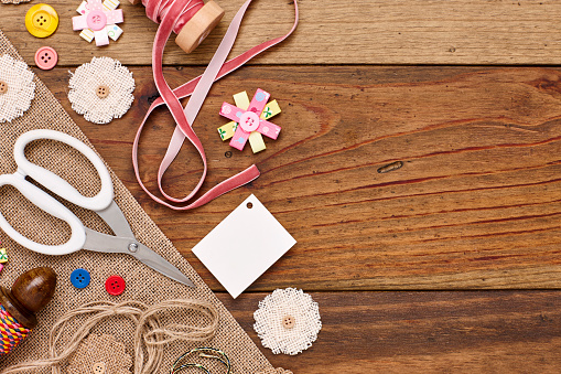 Overhead view of craft products on wooden table. Artificial flowers are placed with art and craft equipment on plank. Empty space on wood can be used for advertisement purpose.