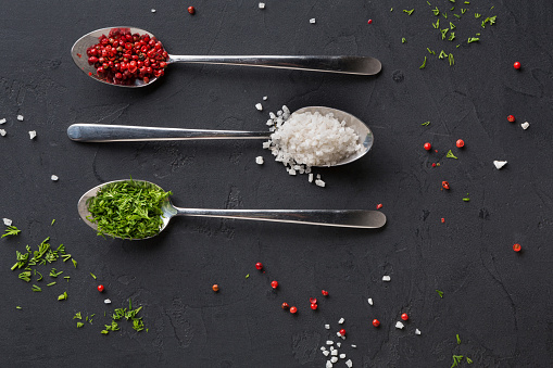 Spices assortment on black background. Salt, peppers and parsley in spoons, closeup, copy space, top view