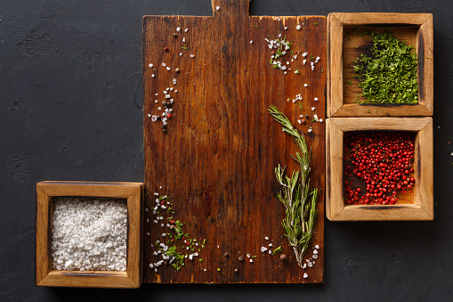 Wooden desk with spices assortment, salt, peppers and parsley in wooden boxes on dark background, top view, copy space.