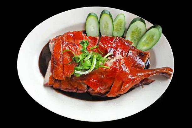 Chinese Roasted duck cutted and served on white dish topped with black gravy herbal sauce isolated on black background with clipping path