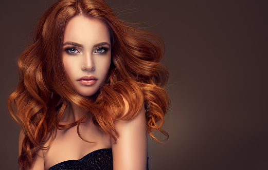Young red haired woman  with voluminous, shiny and wavy hair . Beautiful model with long, dense and curly hairstyle. Flying hair.
