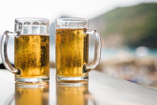 Two glasses of beer on table in restaurant next to the beach