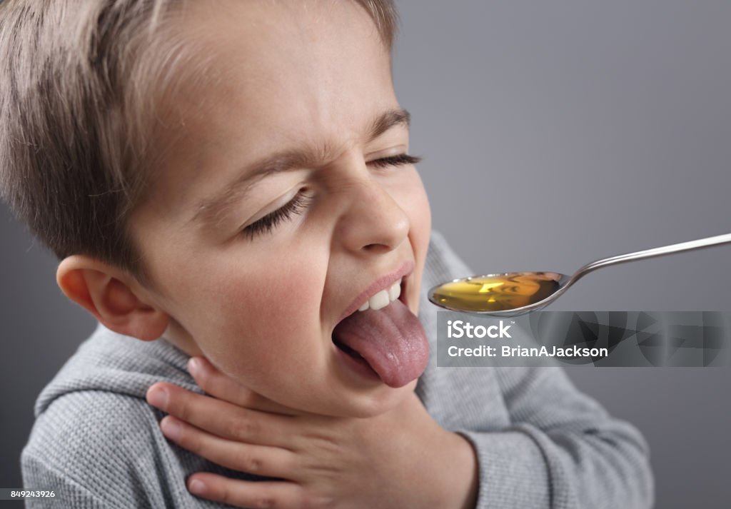 Sick boy taking medicine Sick boy unhappy about taking medicine on a spoon Child Stock Photo