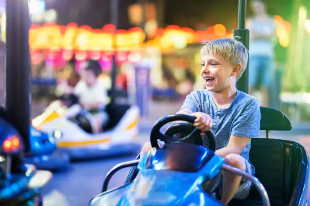 Little boy aged 7 having fun riding bumper car in funfair amusement park. 
