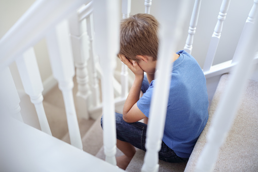 Upset problem child with head in hands sitting on staircase concept for bullying, depression stress or frustration