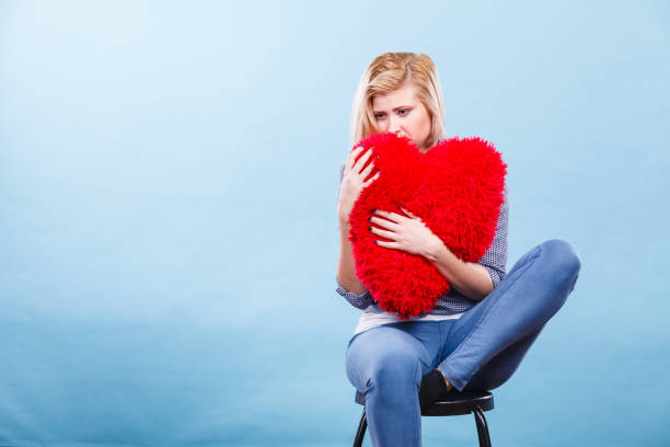 istock Sad woman holding red pillow in heart shape 849250182