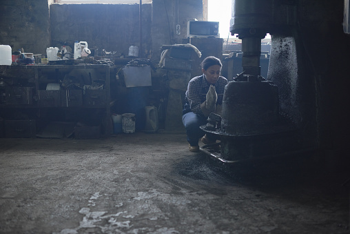 Concentrated young African-American woman crouching while examining furnace or smithy equipment in workshop