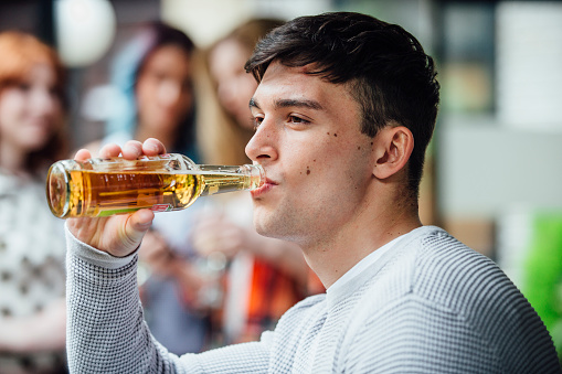 Portrait of a man enjoying a bottle of beer at an outdoor social gathering.