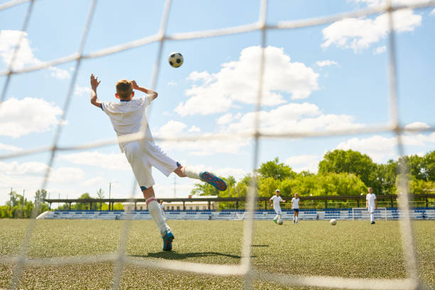 Teenage Goalkeeper Back view portrait of teenage goalkeeper jumping to catch ball during junior football match or practice, shot from behind gate net teen goalie stock pictures, royalty-free photos & images