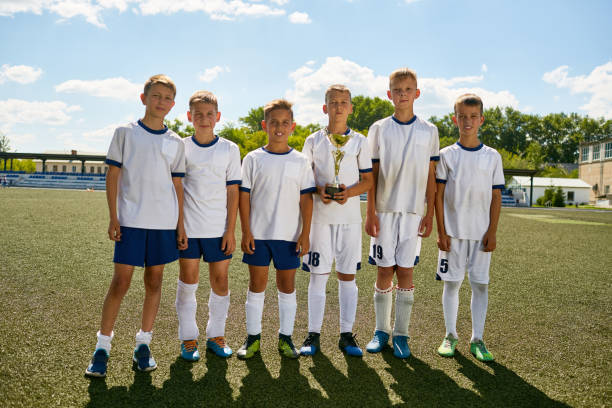 Junior Football Team Posing with Cup Portrait of junior football team posing standing in row and smiling at camera holding champions trophy youth sports competition stock pictures, royalty-free photos & images