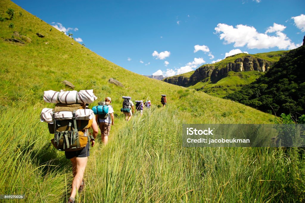 People hiking mountains rucksack boots camping Drakensberg grass hills sky Drakensberg Mountain Range Stock Photo
