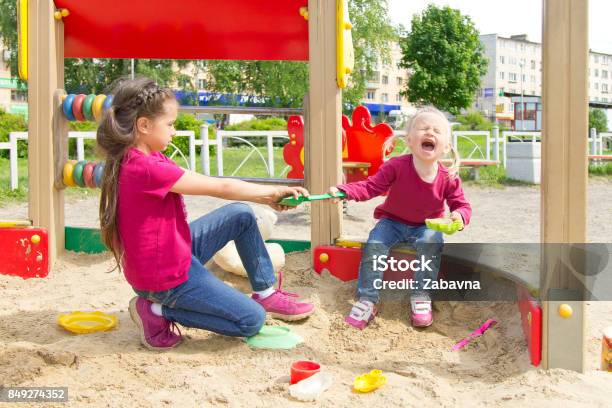 Conflict On The Playground Two Sisters Fighting Over A Toy In The Sandbox Kid Sister Crying All Throat Stock Photo - Download Image Now