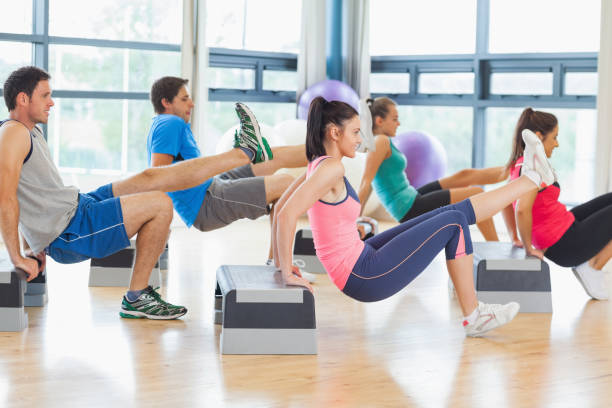 instructor with fitness class performing step aerobics exercise - the next step imagens e fotografias de stock