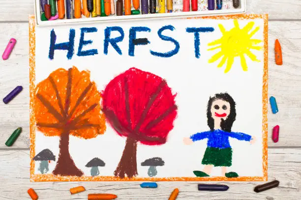 Photo of colorful drawing: Dutch word Autumn, smiling little girl, trees with orange and red leaves,