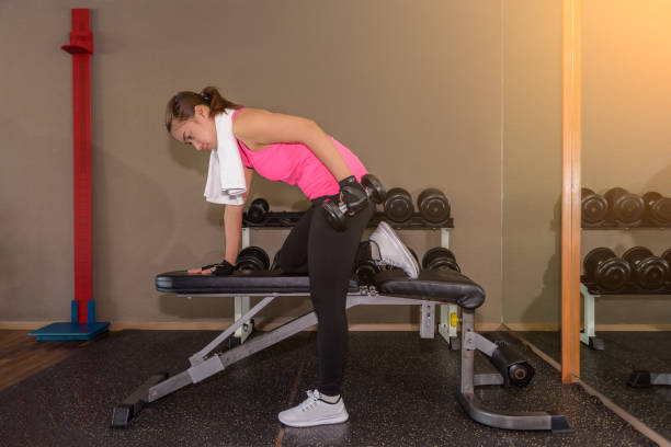 fitness palestra donna allenamento forza sollevare pesi manubrio in bent-over one-arm dumbbell row - arms bent foto e immagini stock
