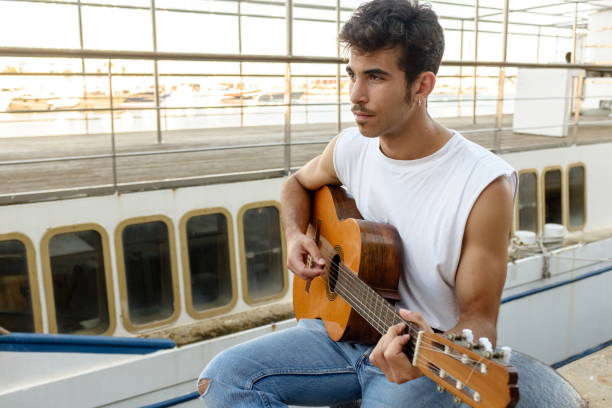 istock Young man playing guitar in harbor 849293710