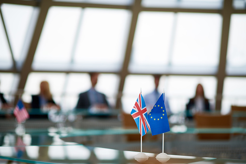 Focus on flags of Great Britain and European Union placed on conference table, business people sitting at table in background