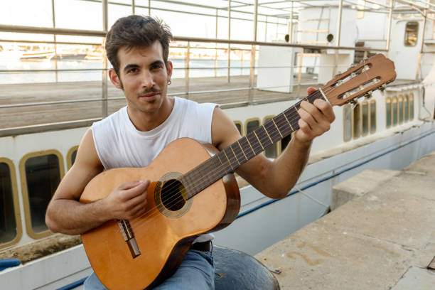 istock Young man playing guitar in harbor 849294286