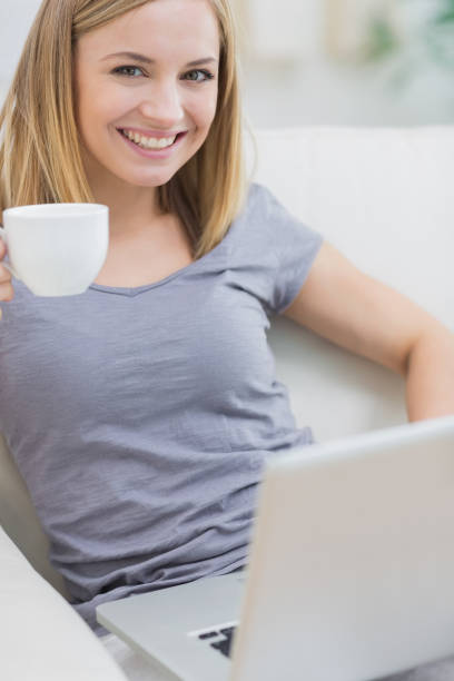 istock Smiling woman with coffee cup using laptop on sofa 849301318