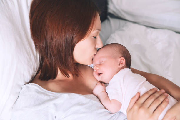 Newborn baby sleeping in the hands of his mother. Mother kissing her newborn baby. Sleeping baby in the hands of his loving mother. Image of happy maternity and co-sleeping. Mom and child's first month of life at home. childbirth photos stock pictures, royalty-free photos & images