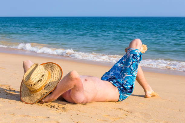 Young man with hat lying on beach with blue sea. My son enjoys his vacation in Albufeira in the country Portugal. He's sunbathing and wearing a straw hat. On this sunny day in summer season tourists come to this place as a travel destination.