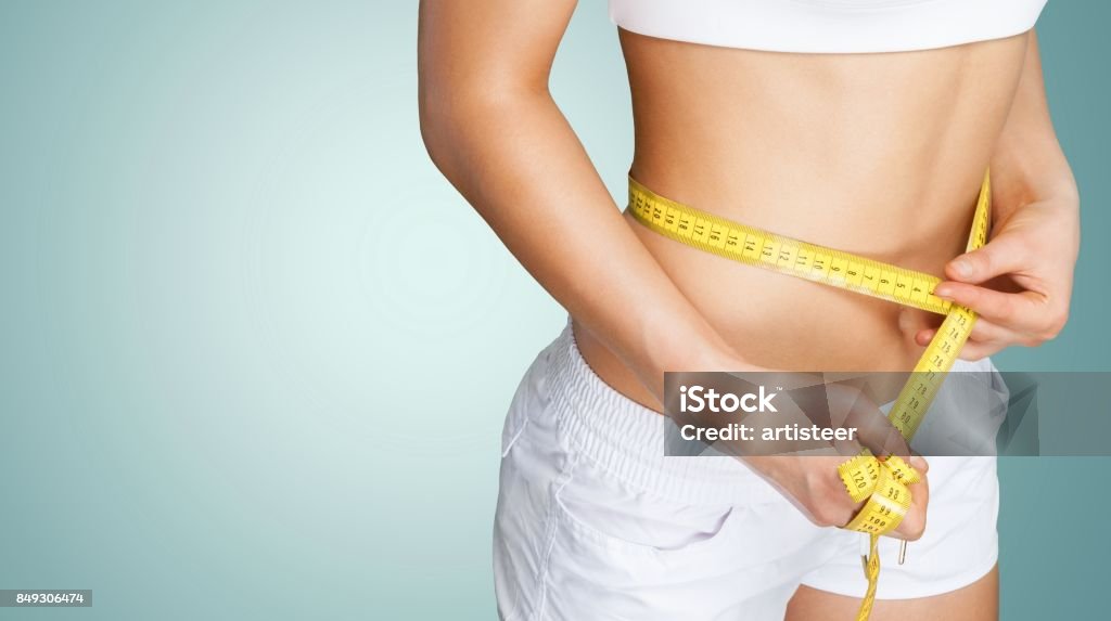 Dieting. Slim young woman measuring her thin waist with a tape measure, close up Burning Stock Photo