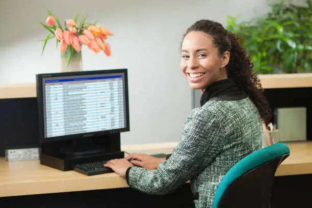 Photo of Black African Decent Bank Teller Working Behind Bank Counter at Retail Bank