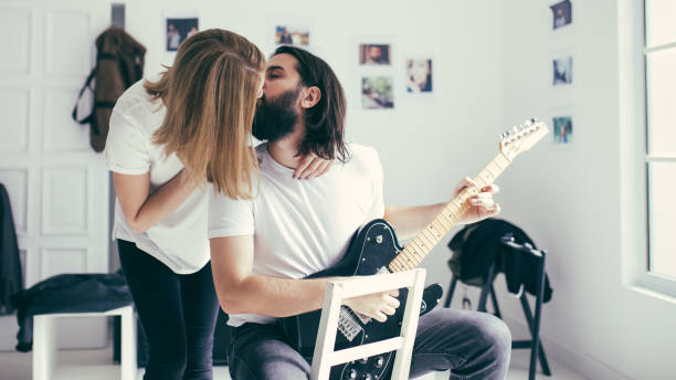 Couple kissing Two people, young heterosexual couple, man playing guitar and the girl is kissing him, in home studio.
 kiss entertainment group stock pictures, royalty-free photos & images