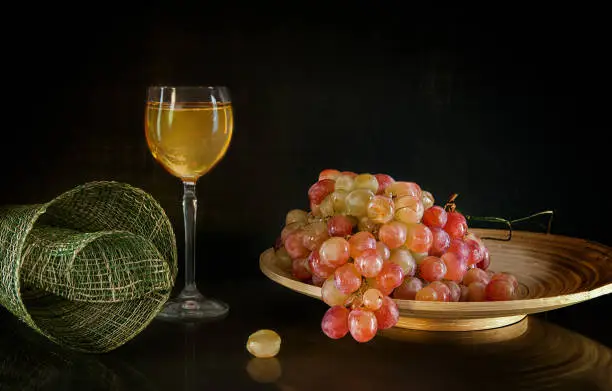 grapes lying on a round plate next to a glass of wine standing on background with reflection