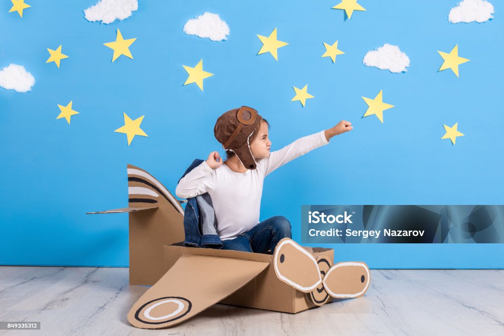 Little child girl in a pilot's costume is playing and dreaming of flying over the clouds Little child girl in a pilot's costume is playing and dreaming of flying over the clouds. Portrait of funny kid on a background of bright blue wall with yellow stars and white clouds Child Stock Photo
