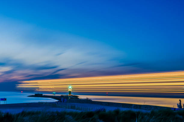 vista nocturna del faro del paseo marítimo de warnemünde en el mar báltico en el puerto con rayas de luz de la nave, rostock alemania - arrival beacon blue nautical vessel fotografías e imágenes de stock