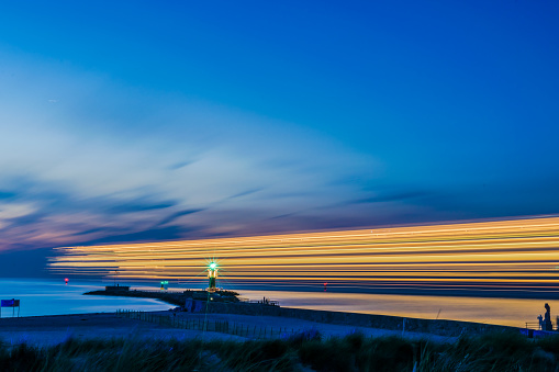 night view of lighthouse of Warnemuende on the Baltic Sea at the harbor with light stripes from ship , Germany Rostock