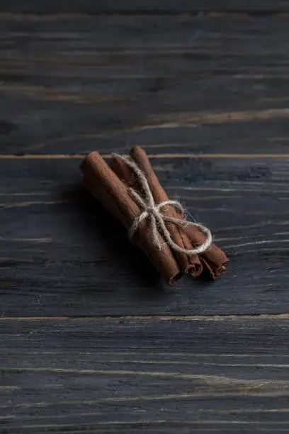 Bunch of cinnamon sticks tied with natural twine on brown wood background