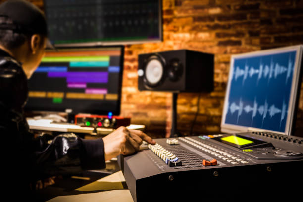 asian male professional sound engineer working in digital recording, broadcasting, editing studio. focus on mixer fader stock photo
