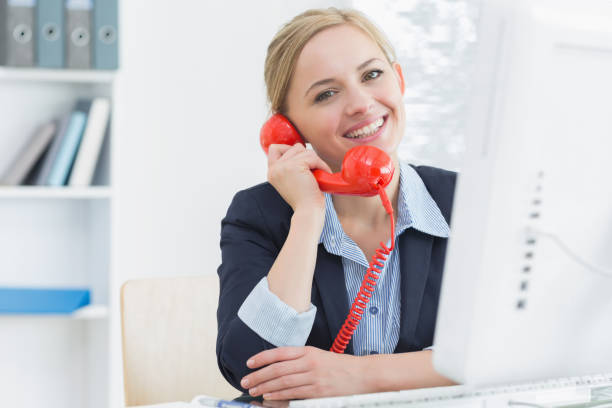 istock Smiling female executive using red land line phone at desk 849404220