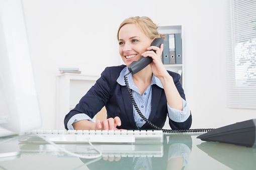 Young female executive using landline phone at desk in office