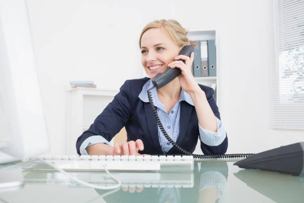 Young female executive using phone at office Young female executive using landline phone at desk in office telephone receiver stock pictures, royalty-free photos & images