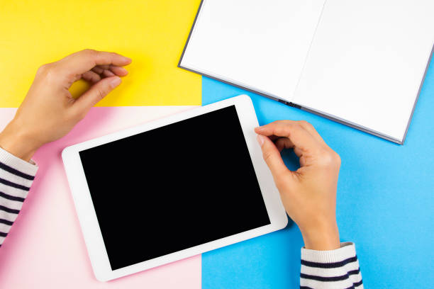 istock Female hands with tablet computer and open notebook over yellow, blue and pink background. 849427540