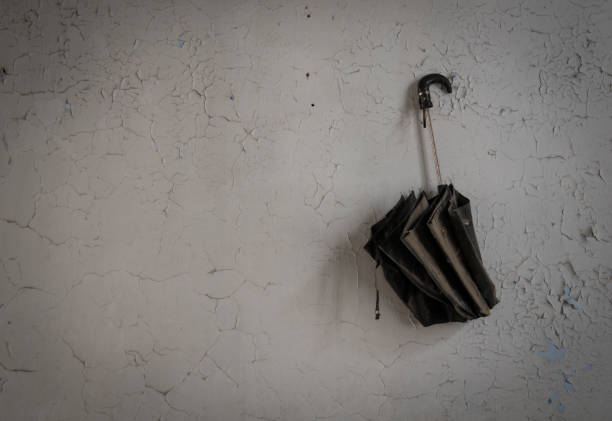 Old black rain umbrella hanging on a damaged white wall of an abandoned room