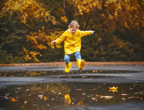 Photo of happy child girl with an umbrella and rubber boots in puddle  on autumn walk