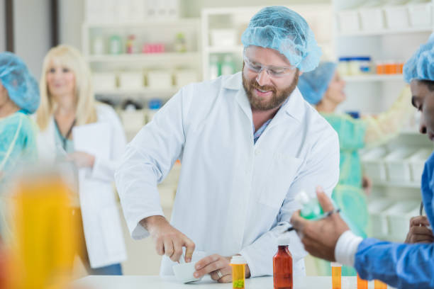 Bearded male pharmacist mixes patient's specialty medication Smiling mid adult Caucasian male pharmacist uses a mortar and pestle to mix up a specialty medication for a patient. His colleagues are working around him. pharmaceutical compounding stock pictures, royalty-free photos & images