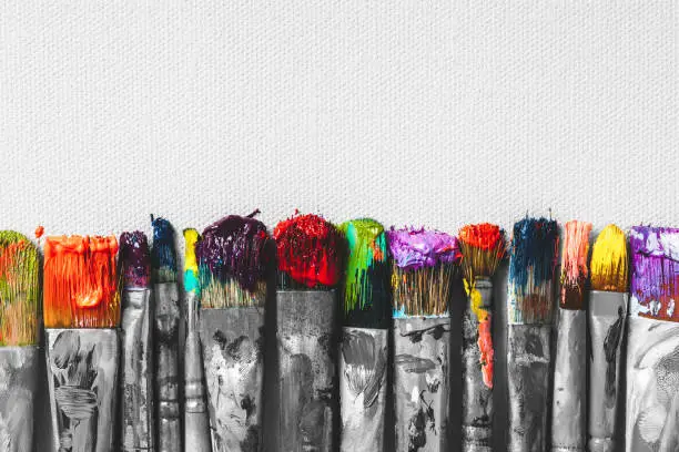 Row of artist paintbrushes with colorful bristle closeup on artistic canvas background, retro black and white stylized.