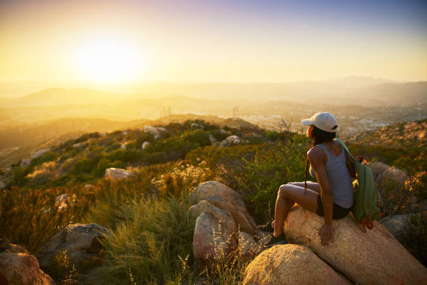 Rear view of woman hiker sitting on rock on top of hill Rear view of woman hiker sitting on rock on top of hill while looking at sunset over San Diego California southern california stock pictures, royalty-free photos & images