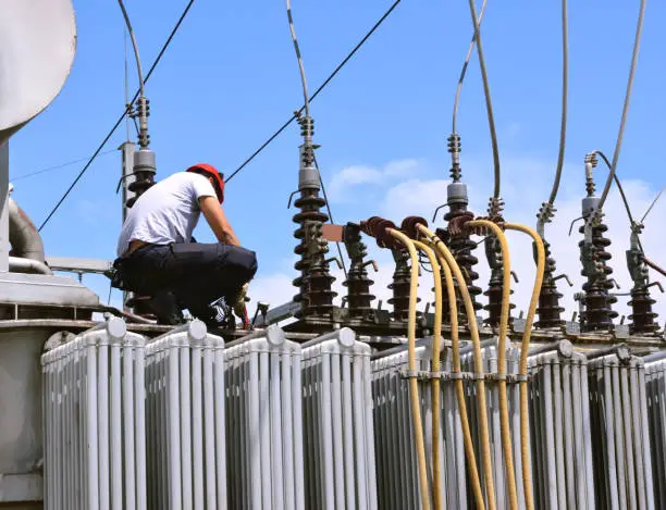 Manual worker in protective workwear and hard hat repairing electricity equipment in power plant