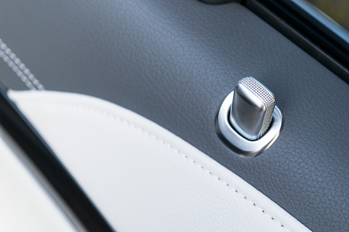 Door handle with lock contol buttons of a luxury passenger car. Black leather interior of the luxury modern car. Modern car interior details