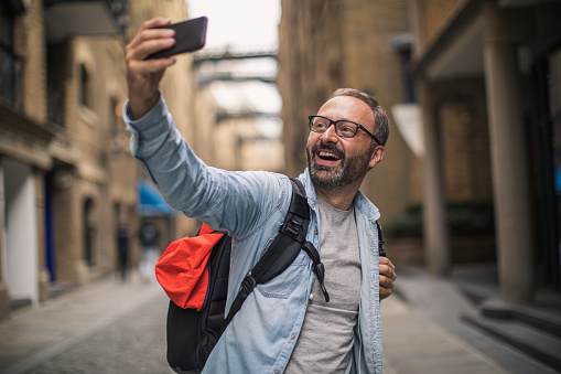 Tourist man standing on the city street and making selfie